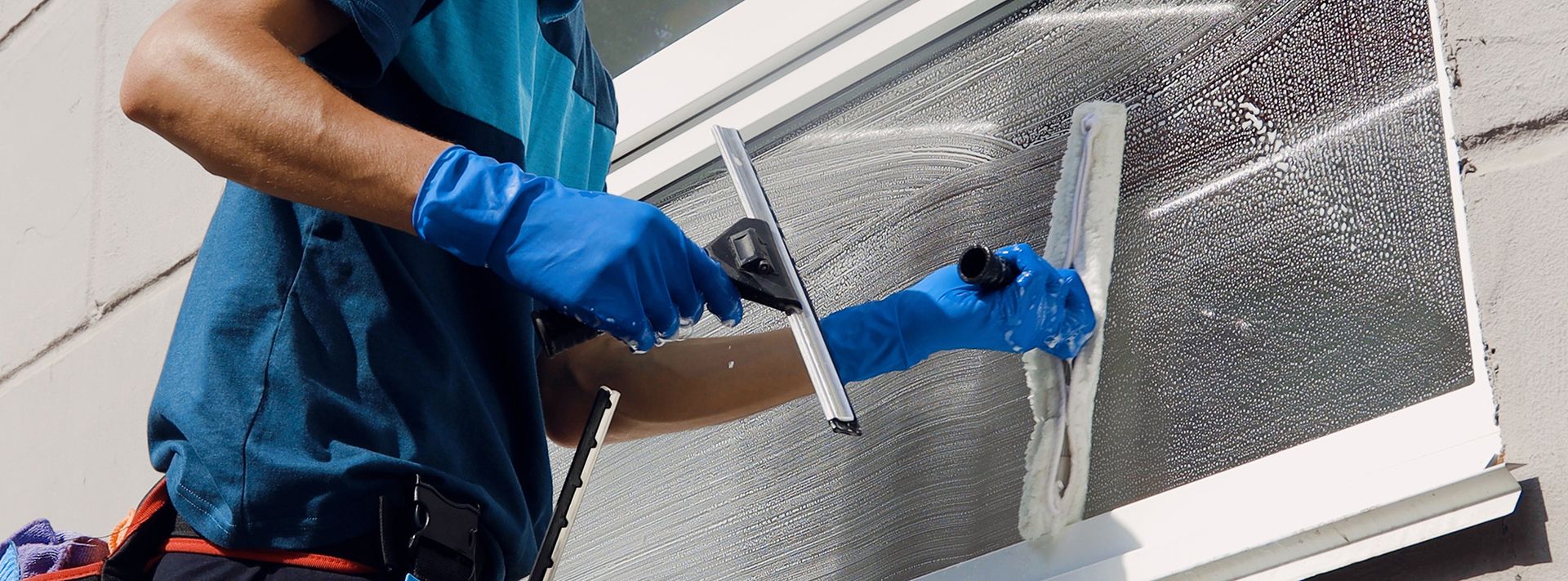 Ein Mann trägt blaue Handschuhe und säubert ein Fenster.